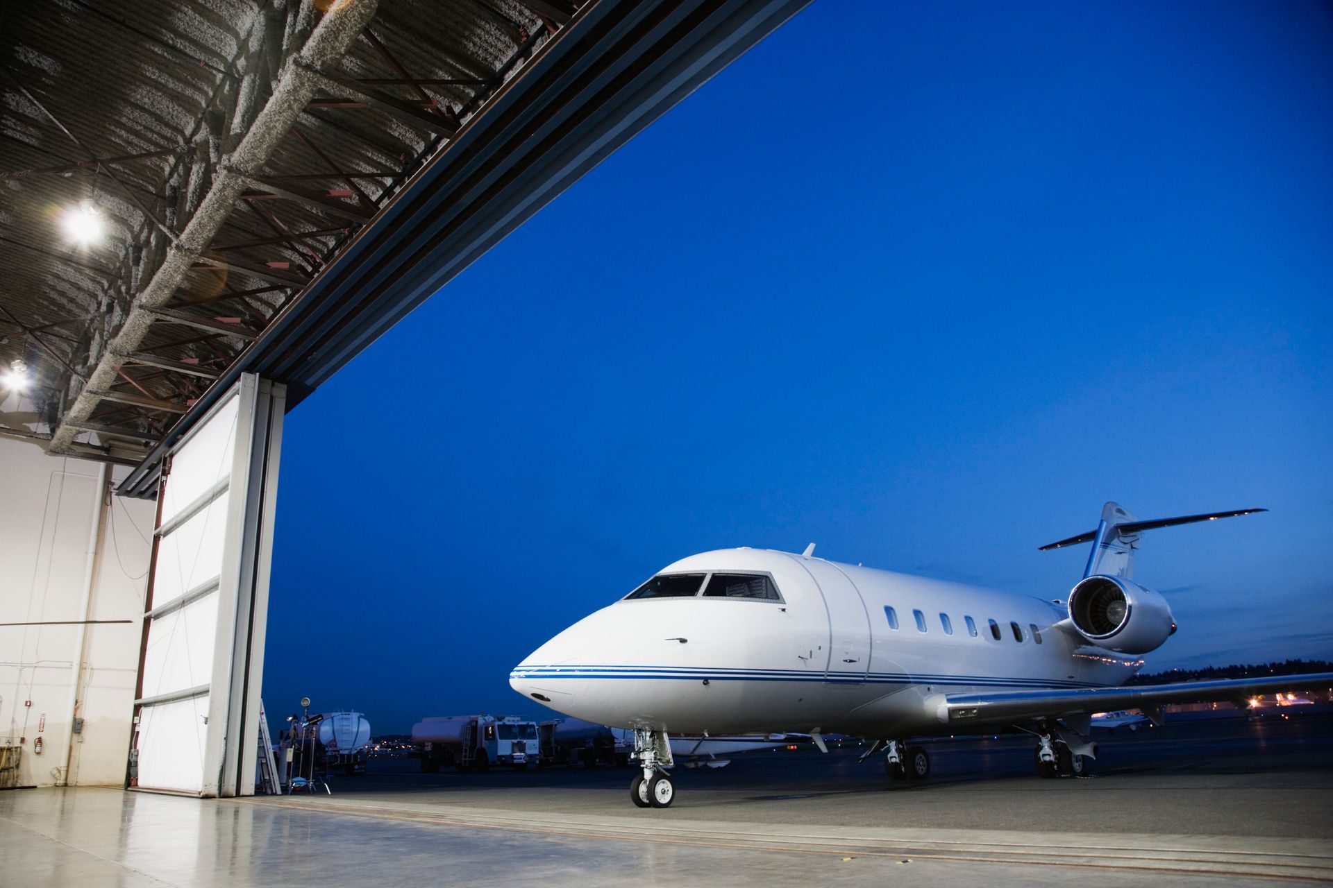 White private jet parked in an open hangar against a blue twilight sky.