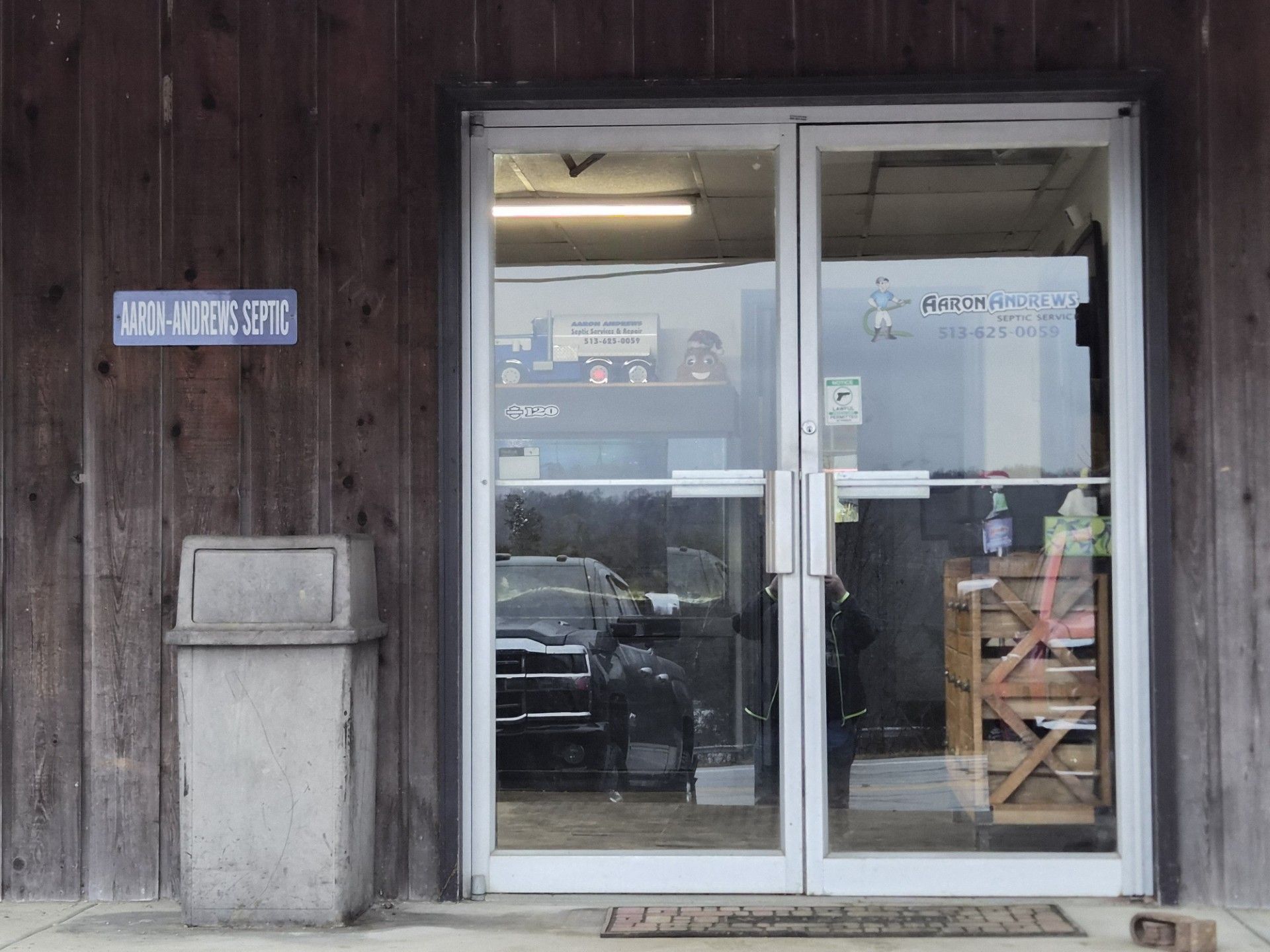 Entrance of a business with glass doors, wooden siding, and a trash can on the side.
