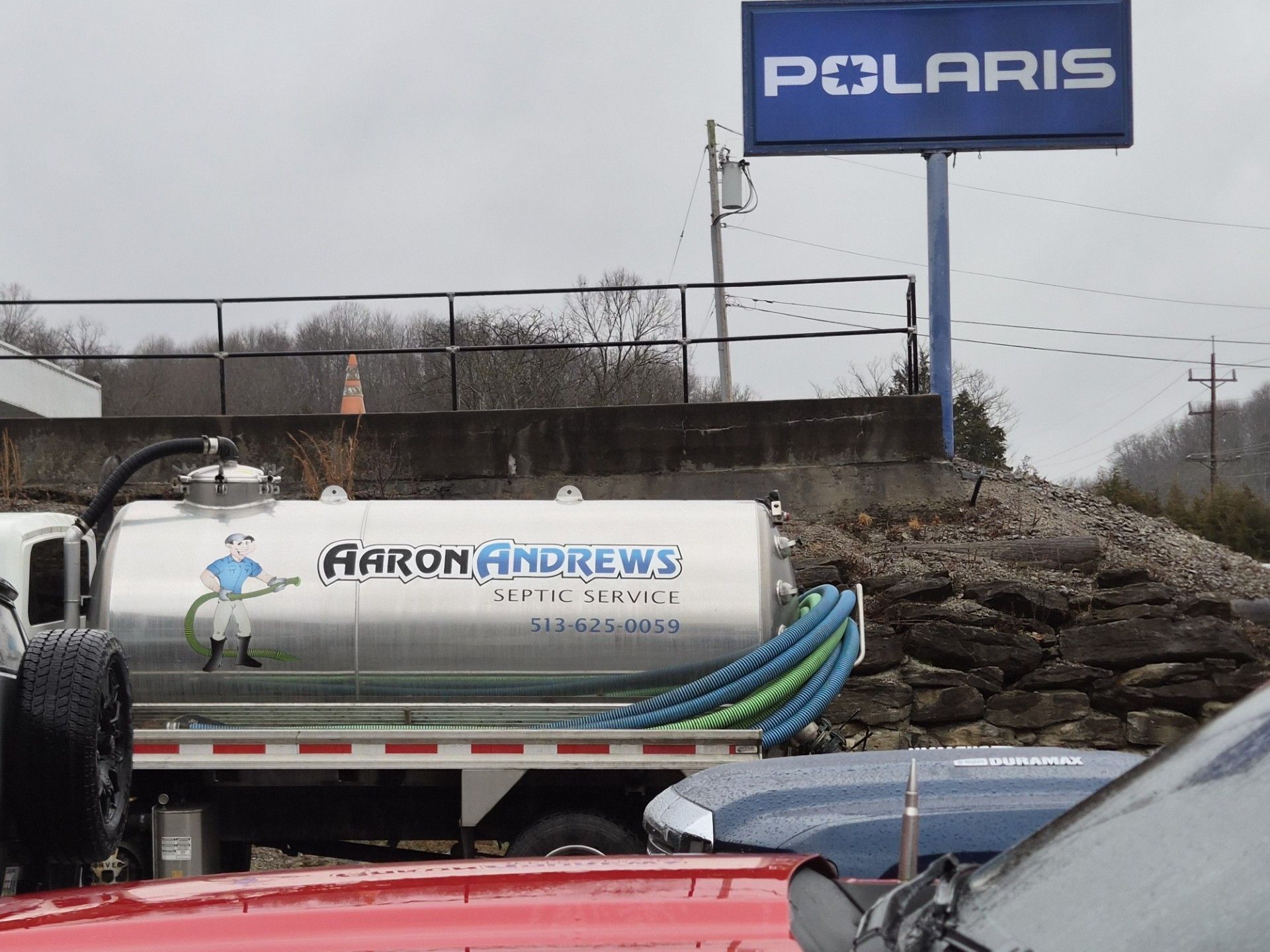 Septic tank truck in front of a Polaris sign, presumably at a dealership. Cloudy sky.
