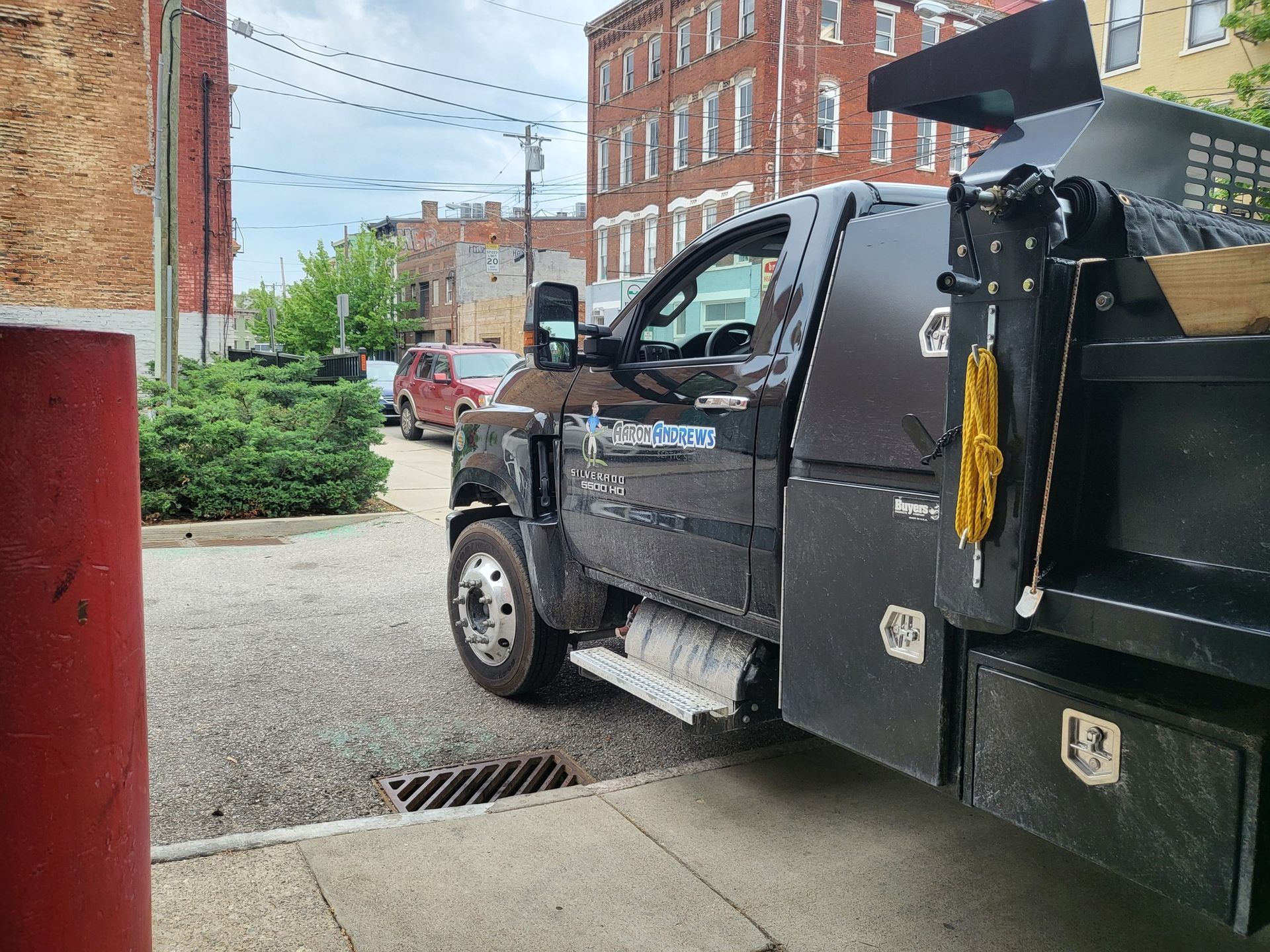 Black dump truck parked on a city street; brick buildings in background.