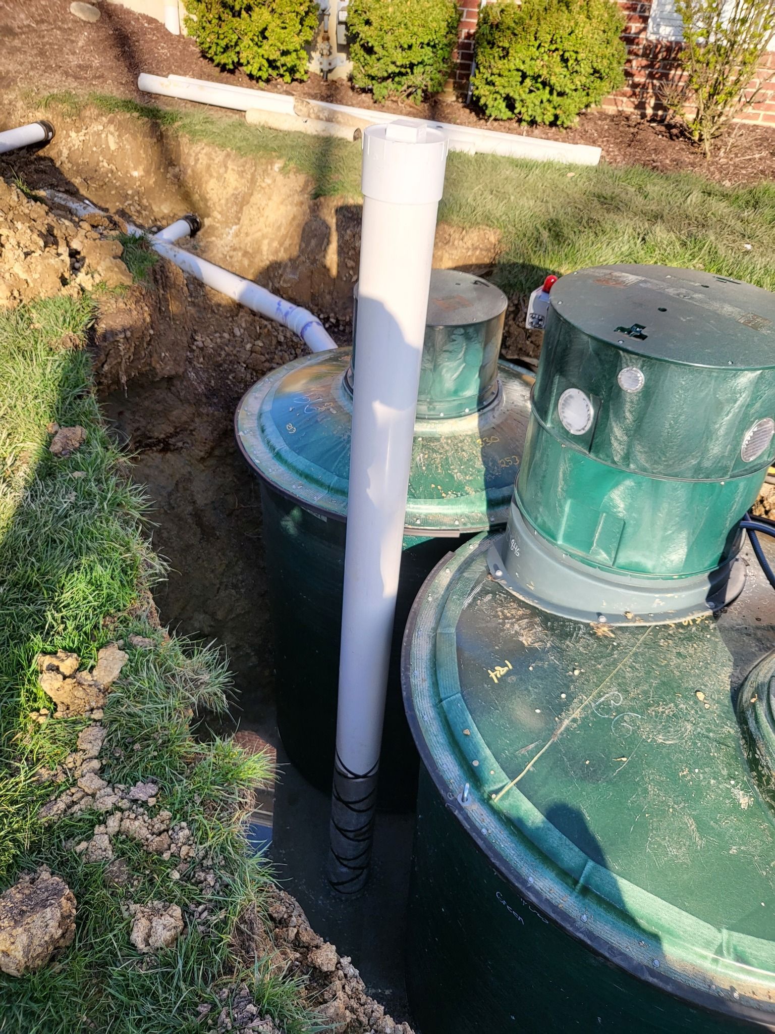 Green septic tanks with white PVC pipe and gray drainage pipes in a trench.