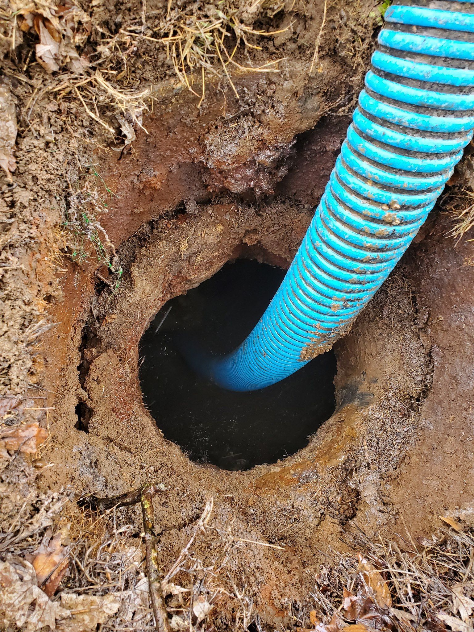 Hole in ground with blue corrugated pipe extending into it; dirt and debris around the opening.