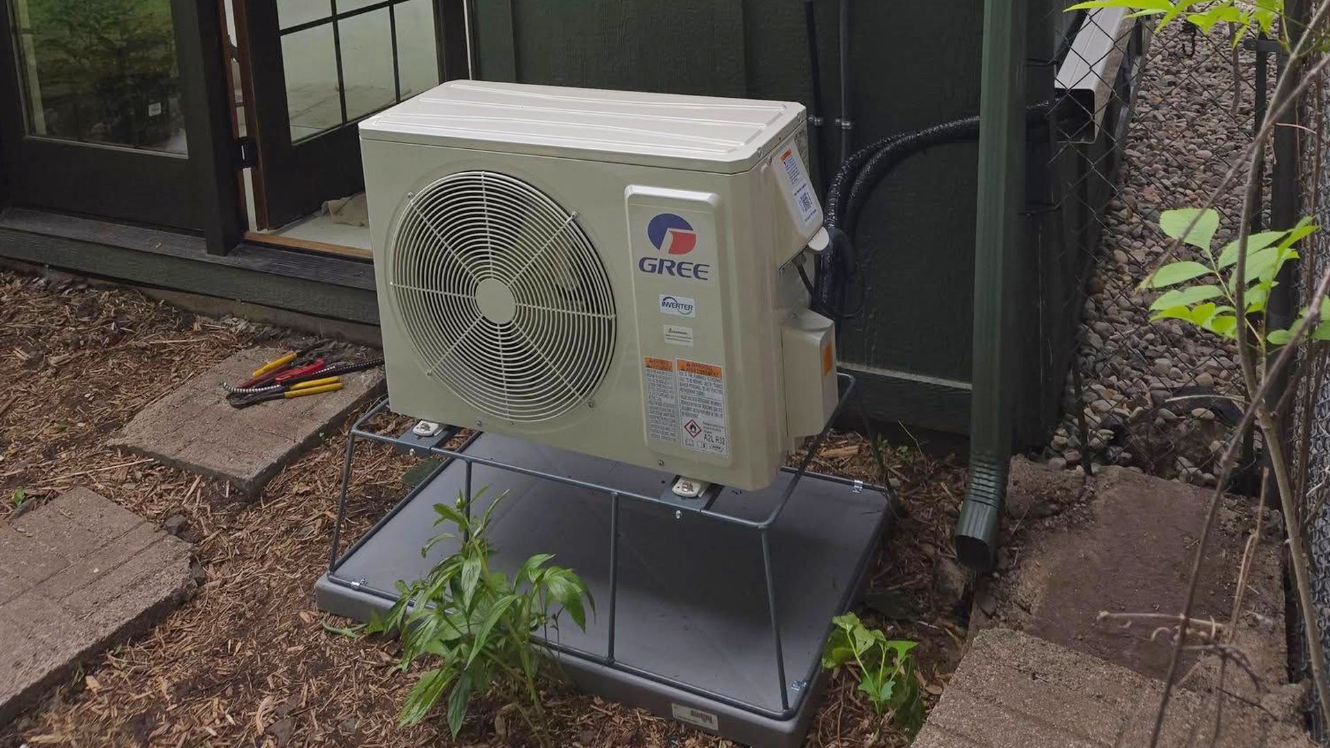 Outdoor air conditioning unit, beige and silver, on a metal platform, near a building entrance.