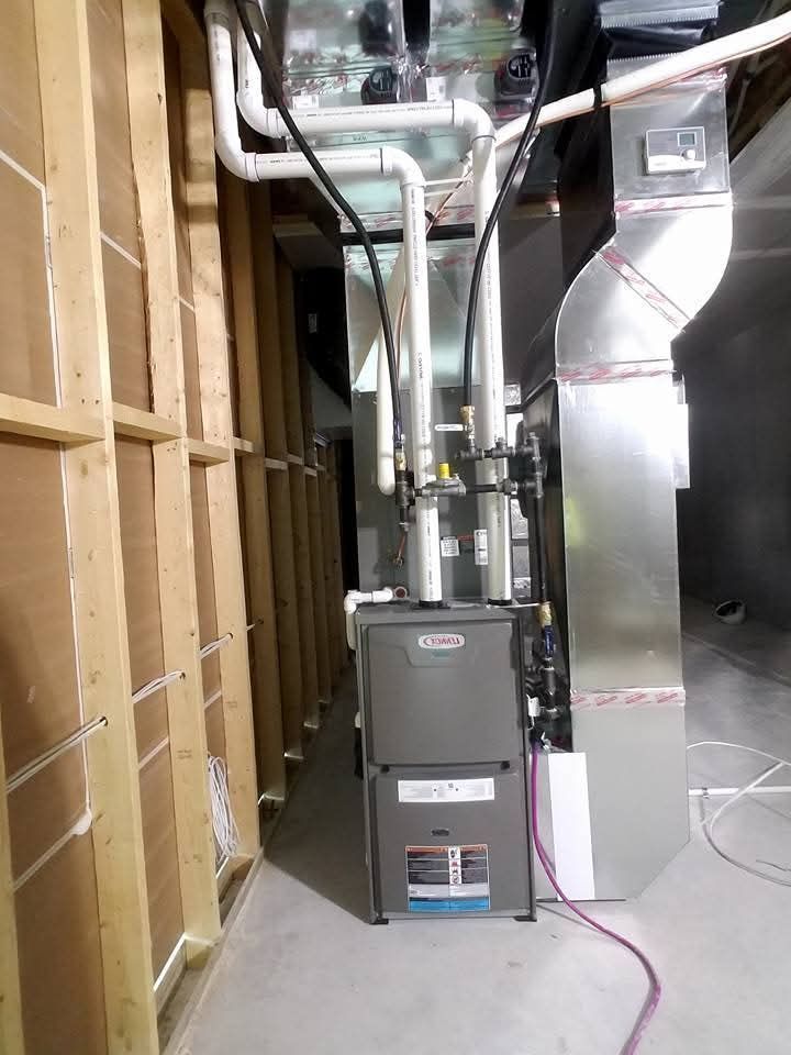 Furnace installed in a narrow room with ductwork, piping, and wooden framing. Gray and silver components.