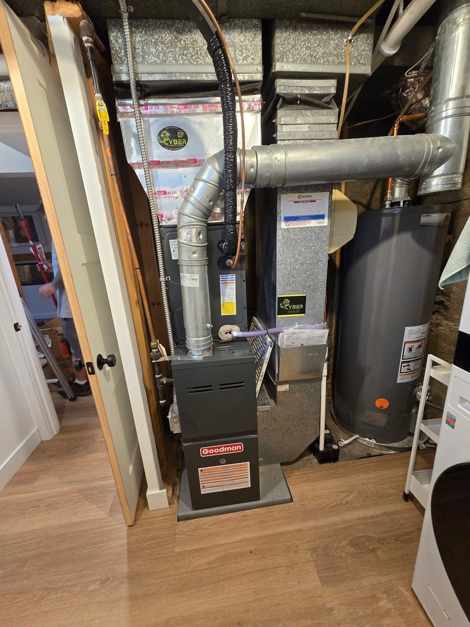 A furnace, ductwork, and water heater in a basement. Brown floor. Gray metal and silver ducting.