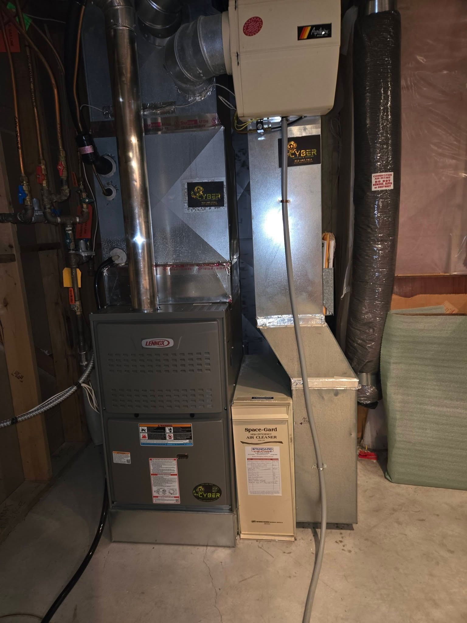 Furnace and humidifier in a basement. The Lennox furnace is dark grey. Ductwork and wiring visible.