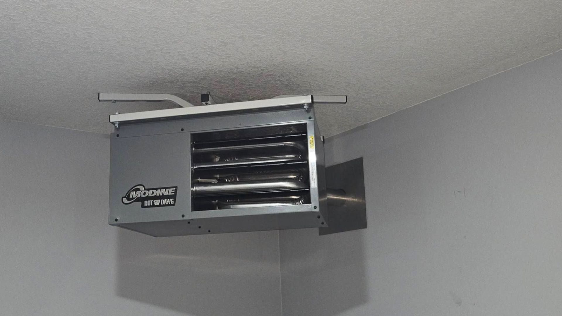 Garage heater mounted on the ceiling. Gray metal box with heating elements visible, installed in a corner.
