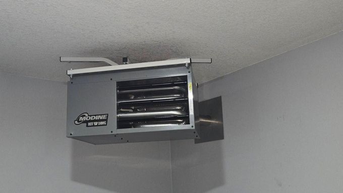 Garage heater mounted on the ceiling. Gray metal box with heating elements visible, installed in a corner.
