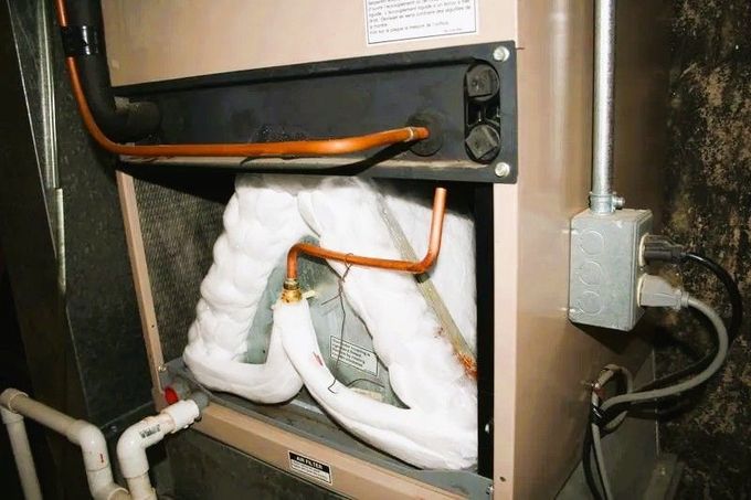 A frozen evaporator coil inside an HVAC unit, coated in white ice, with exposed copper piping and electrical connections.
