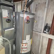 A tall, gray water heater with a plumbing system, positioned indoors.