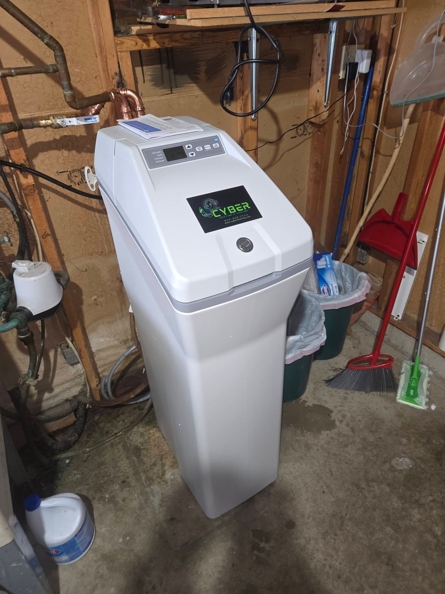 Water softener system in a garage setting with cleaning supplies nearby.