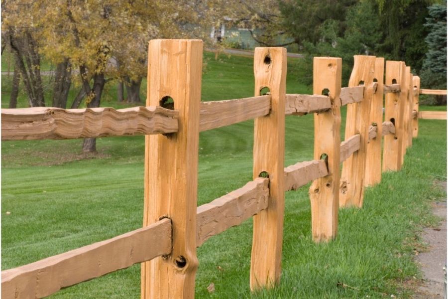 Wooden split-rail fence in a grassy yard, with posts and rails visible.