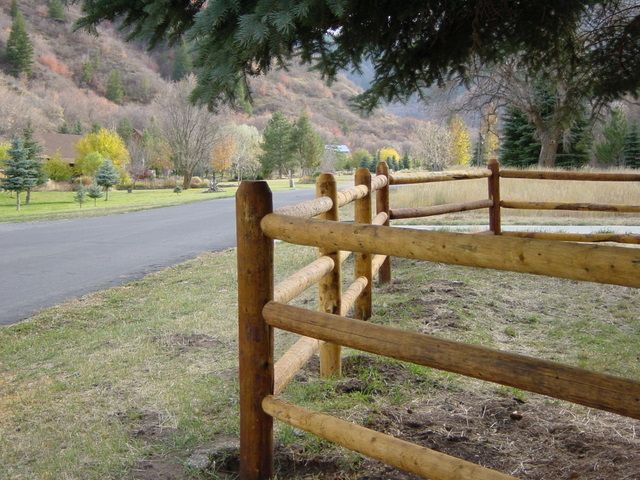 Wooden split-rail fence alongside a road with a mountain and trees in the background.