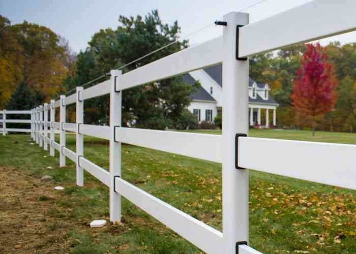White vinyl fence in a grassy yard, with a house in the background and a colorful tree.
