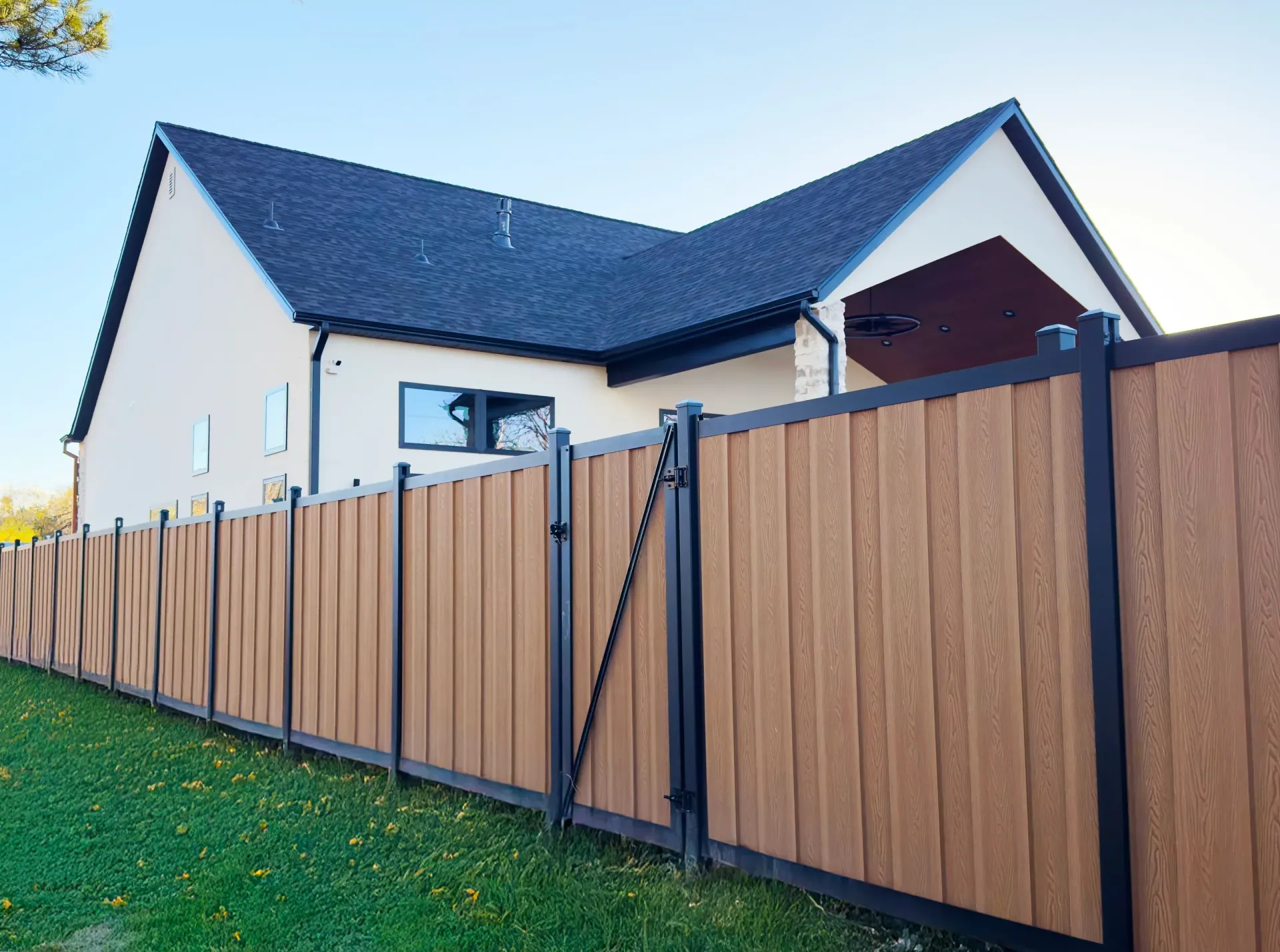 Tan vertical plank fence with black frame in front of a house with a dark roof.