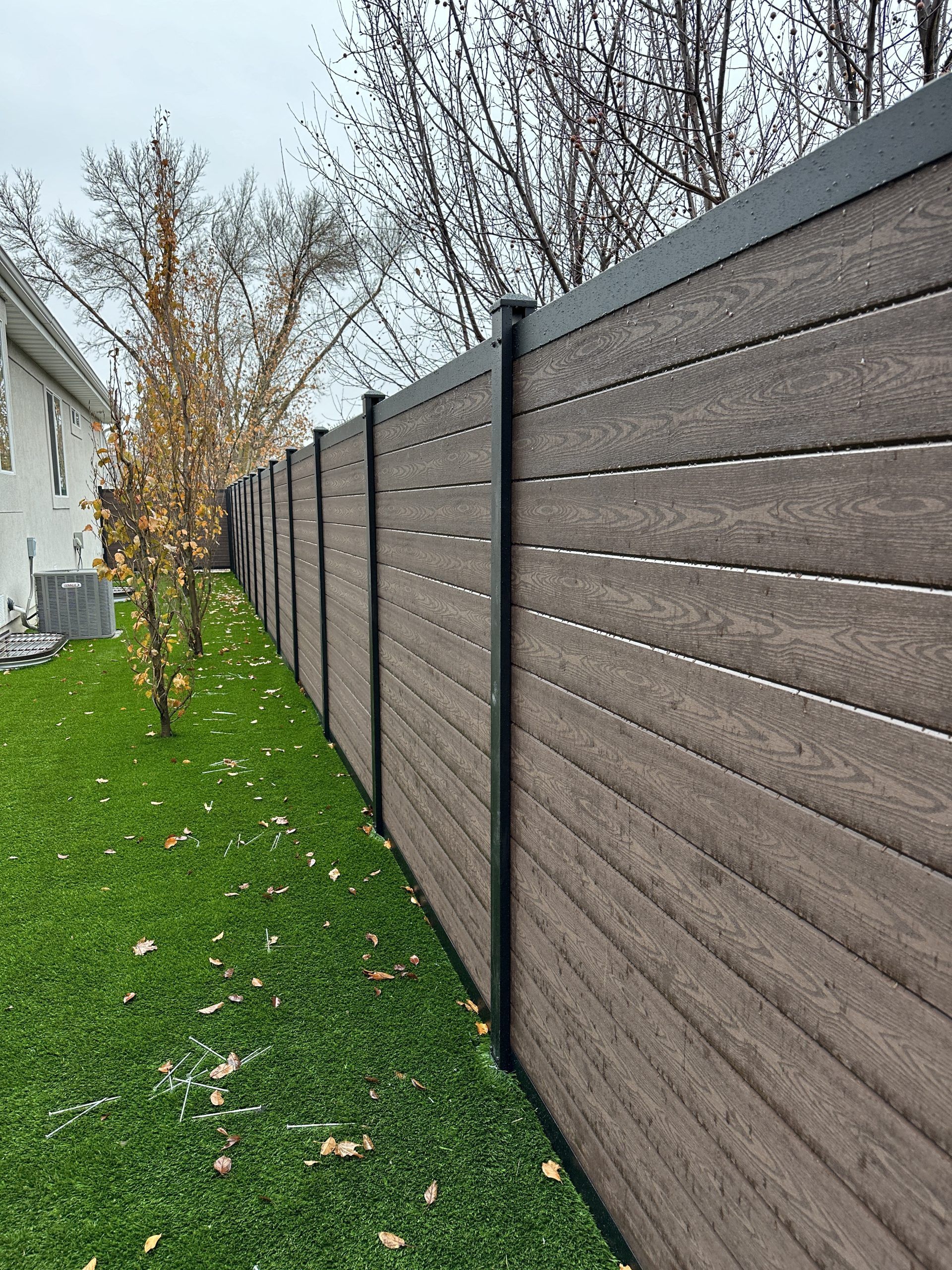 Brown horizontal plank fence with black posts, along a green lawn.