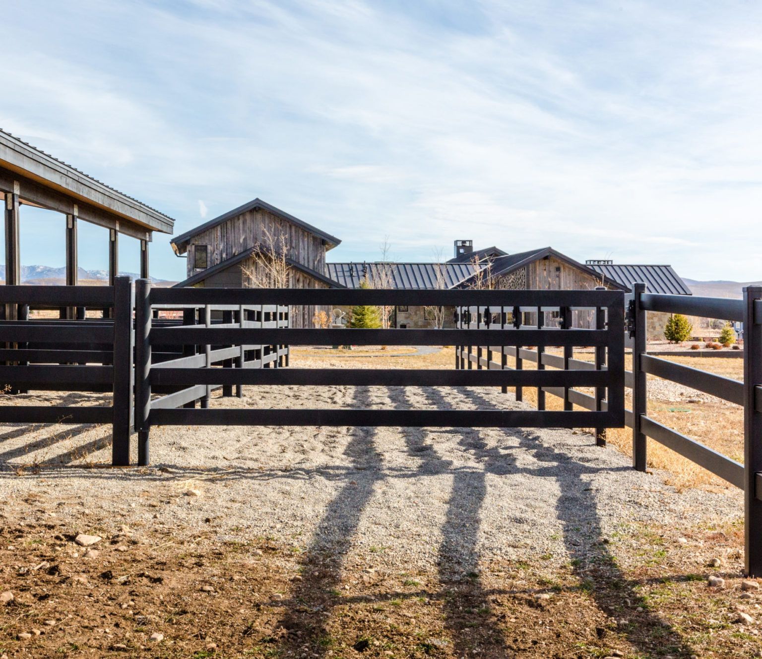 Black fence and gates in front of rustic wooden buildings, outdoor setting, sunny day.