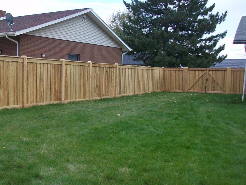 Wooden fence enclosing a grassy backyard, with a brick house and tree in the background.