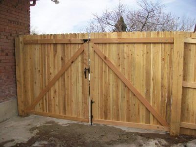 Wooden double gate in a wooden fence with diagonal supports; brick wall background.