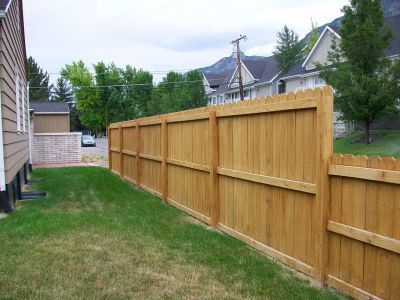 Wooden fence along a grassy yard, with houses and trees in the background.