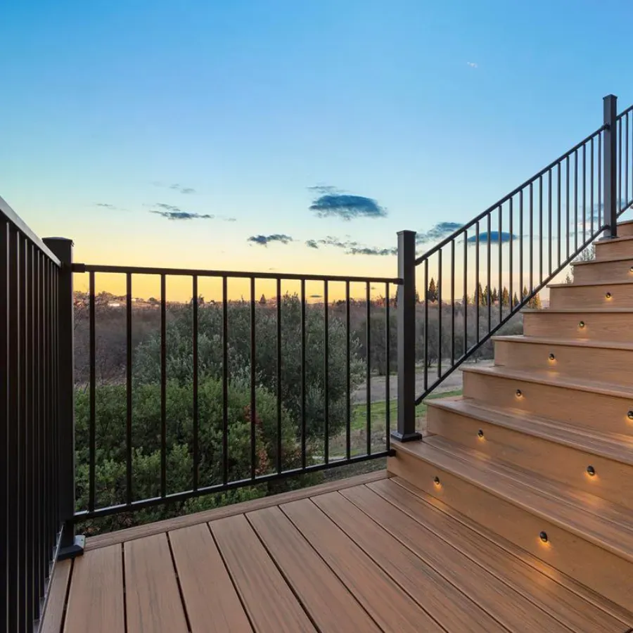 Deck with steps, black railing, and built-in lights, overlooking trees and a colorful sunset.