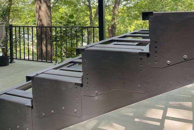 Black metal staircase leading up to a deck with a black railing, set outdoors.