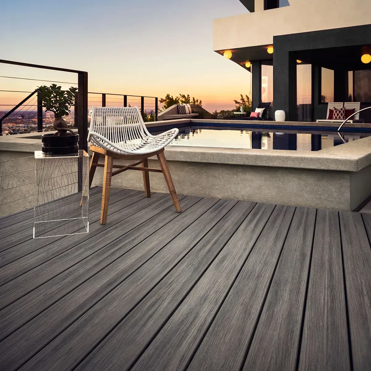 Composite deck with a white chair, overlooking a pool and cityscape at sunset.