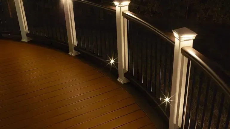 Lit deck railing with warm-toned decking; lights on posts and lower railing for nighttime visibility.