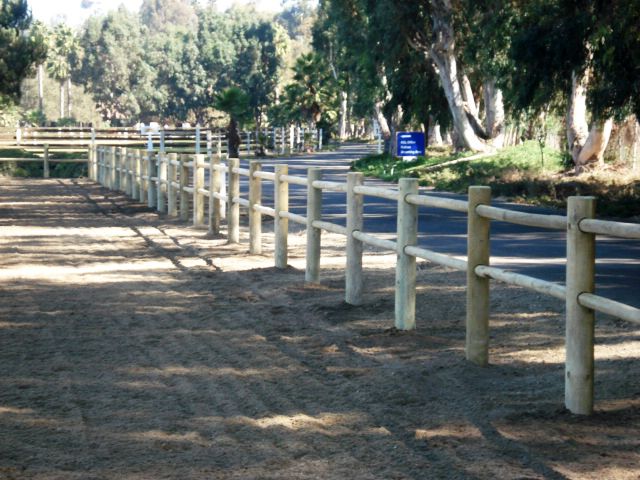 Wooden fence along a road, in a park-like setting. Trees in the background.