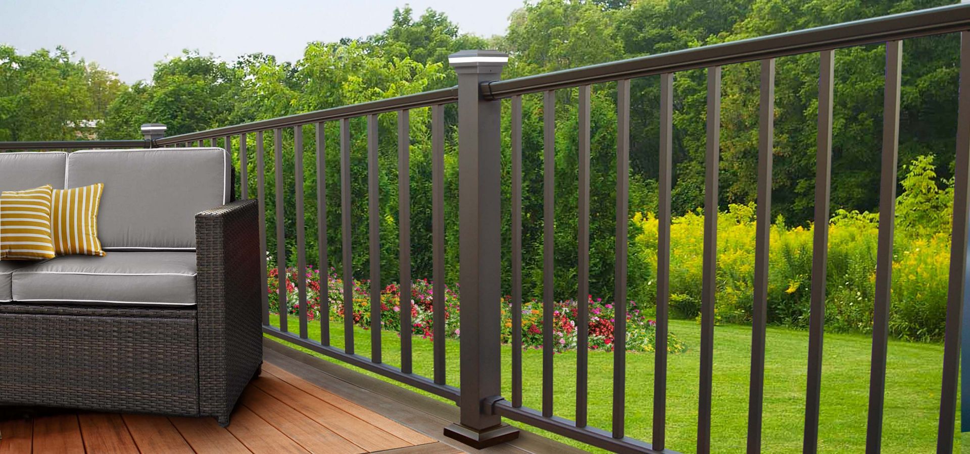 A dark gray deck railing surrounds a patio with gray outdoor furniture and green trees.