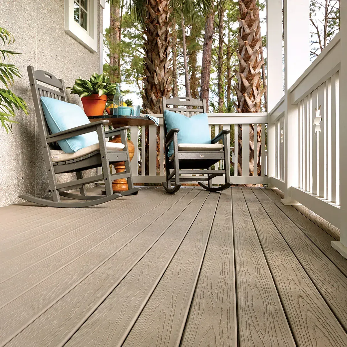 Porch with grey rocking chairs, light brown deck, and view of trees.