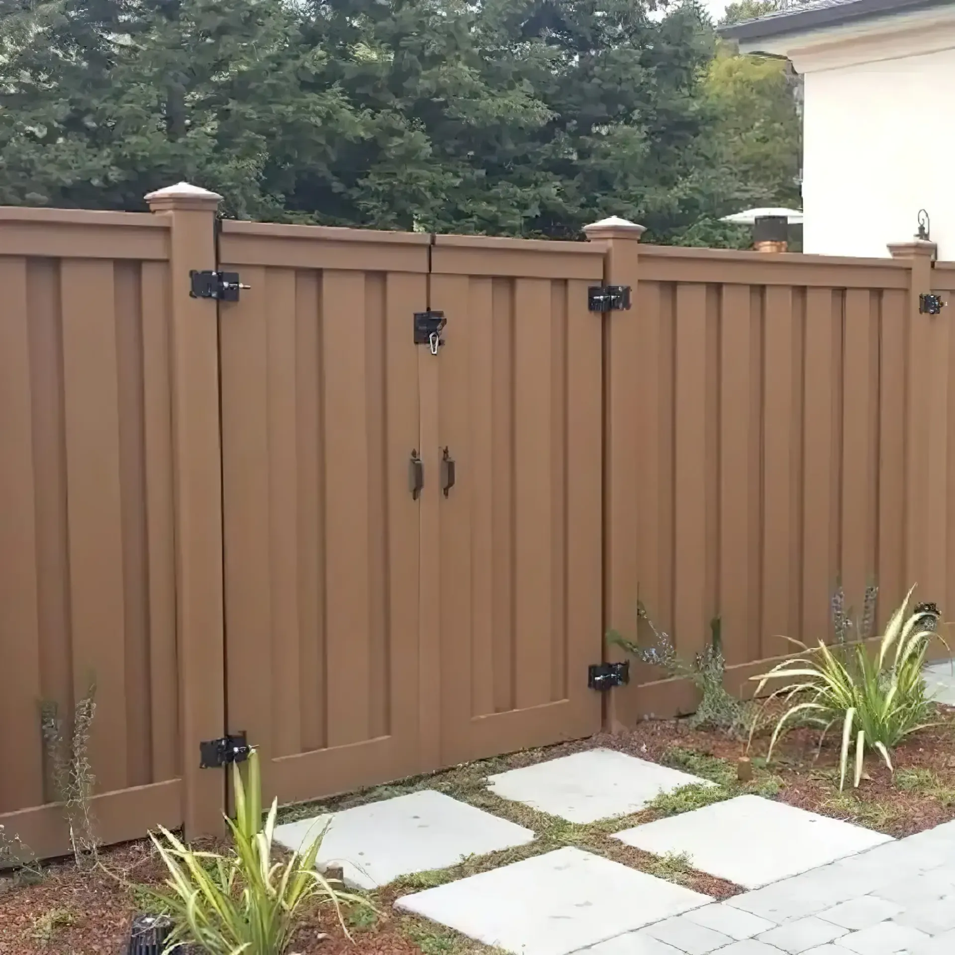 Brown vinyl fence with a gate, plants, and stone pavers.