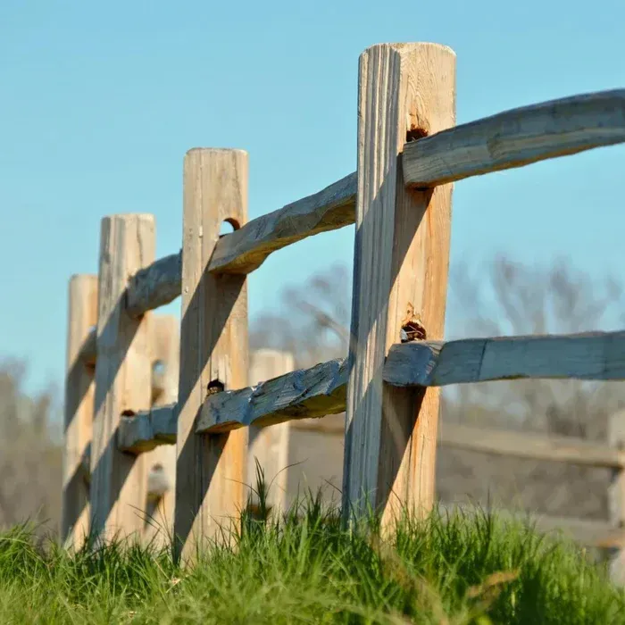 Wooden split-rail fence in a grassy field against a blue sky.