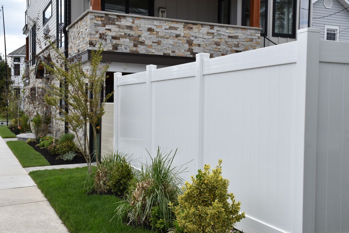 White privacy fence alongside a green lawn, sidewalk, and house with stone accents.