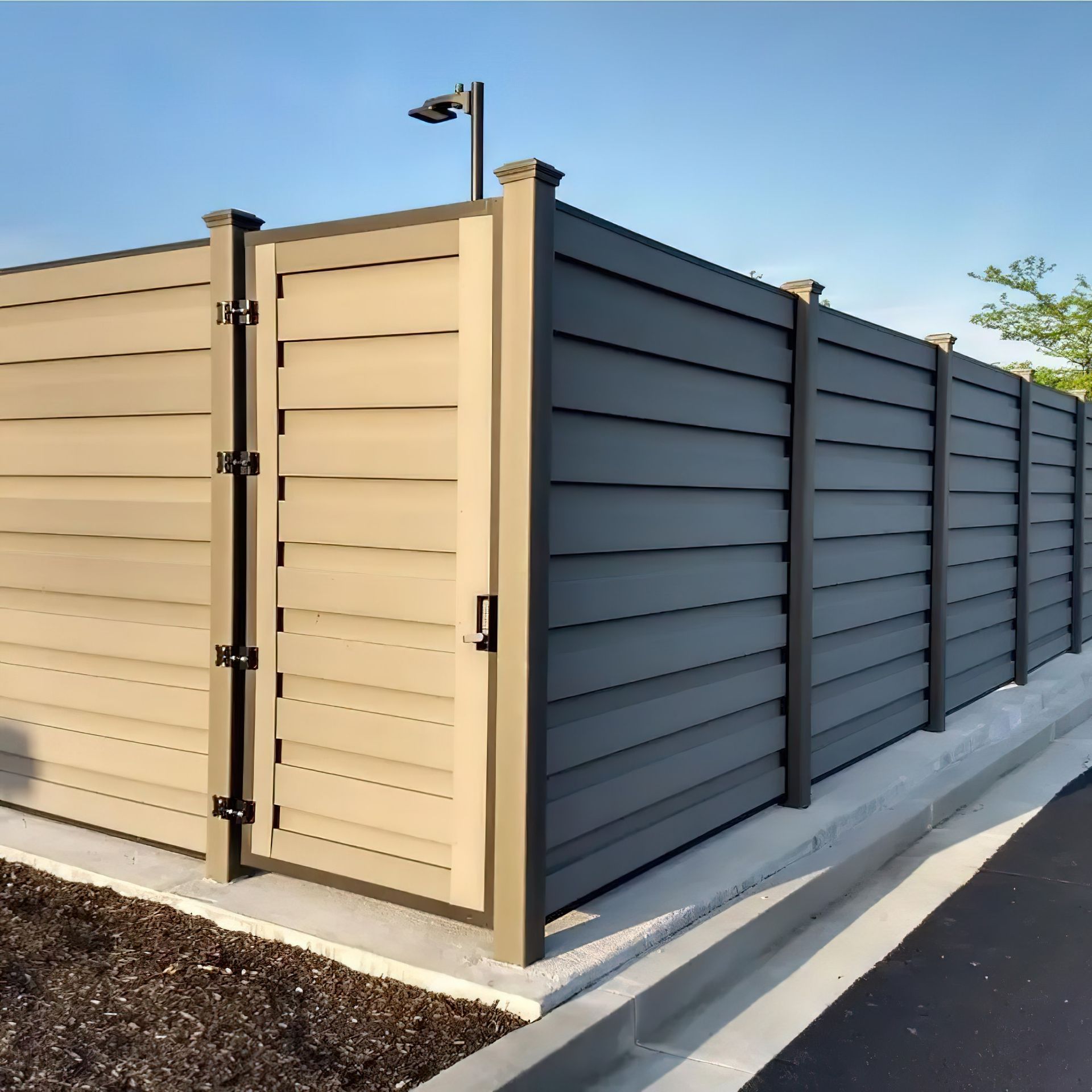 Tan and gray horizontal slat fence with a gate, next to a concrete curb, in daylight.
