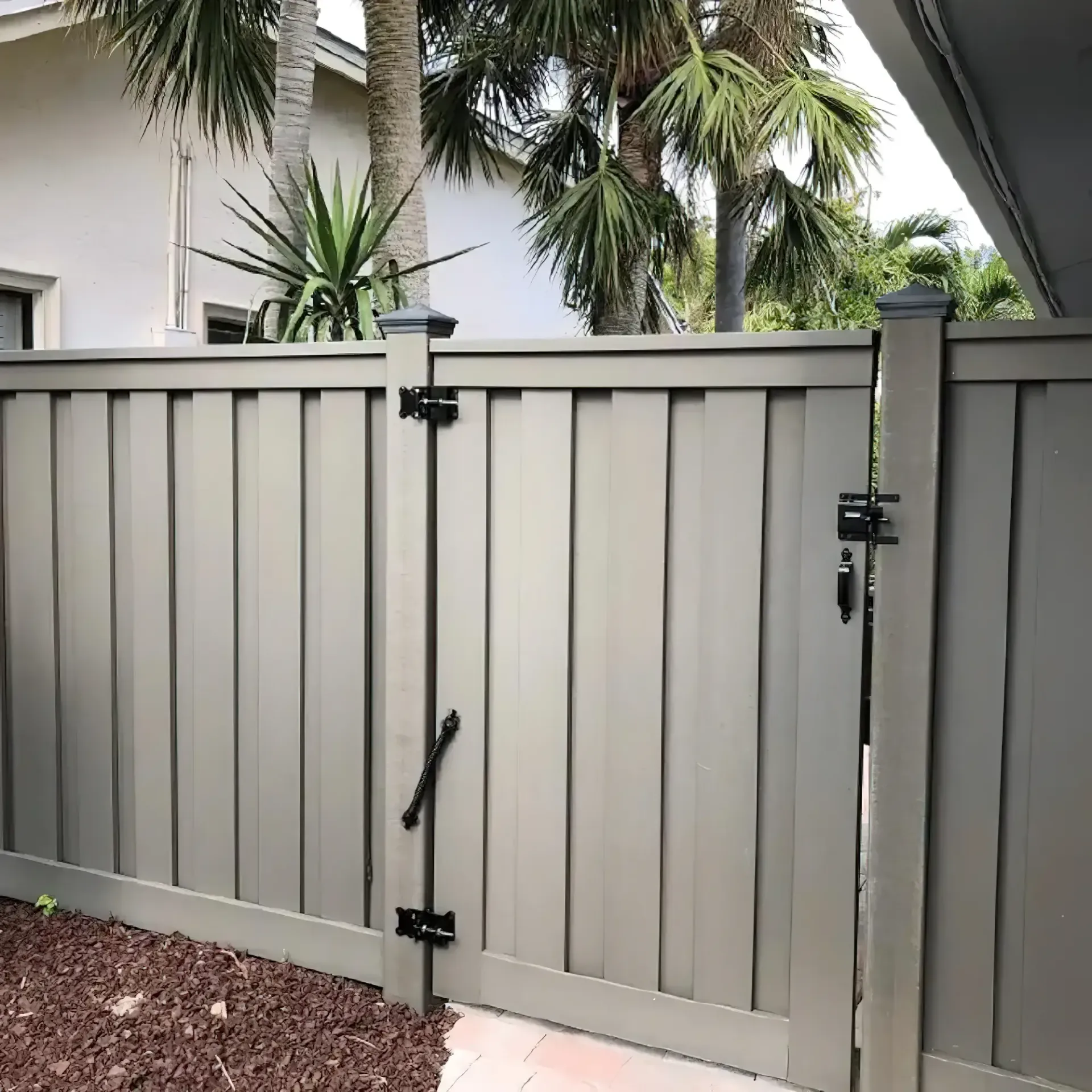 Gray vertical-slat gate with black hardware; outside, near palm trees.
