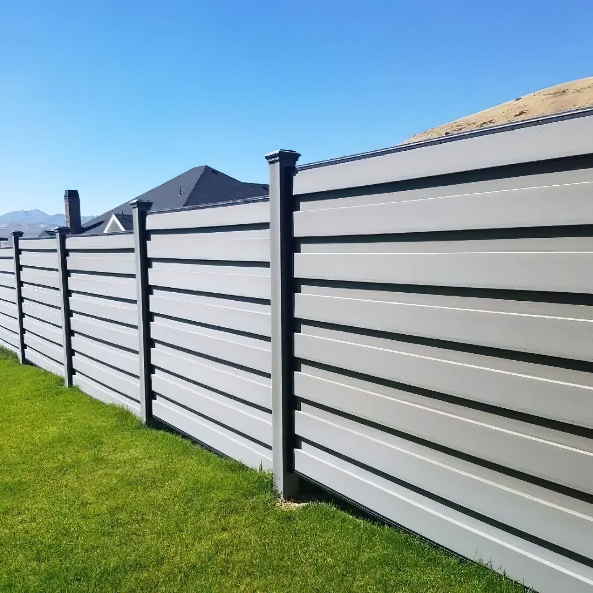 Gray horizontal slat fence in a grassy yard, with blue sky in the background.