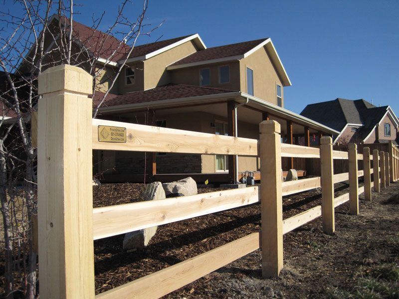 Wooden fence in front of a tan house on a sunny day.