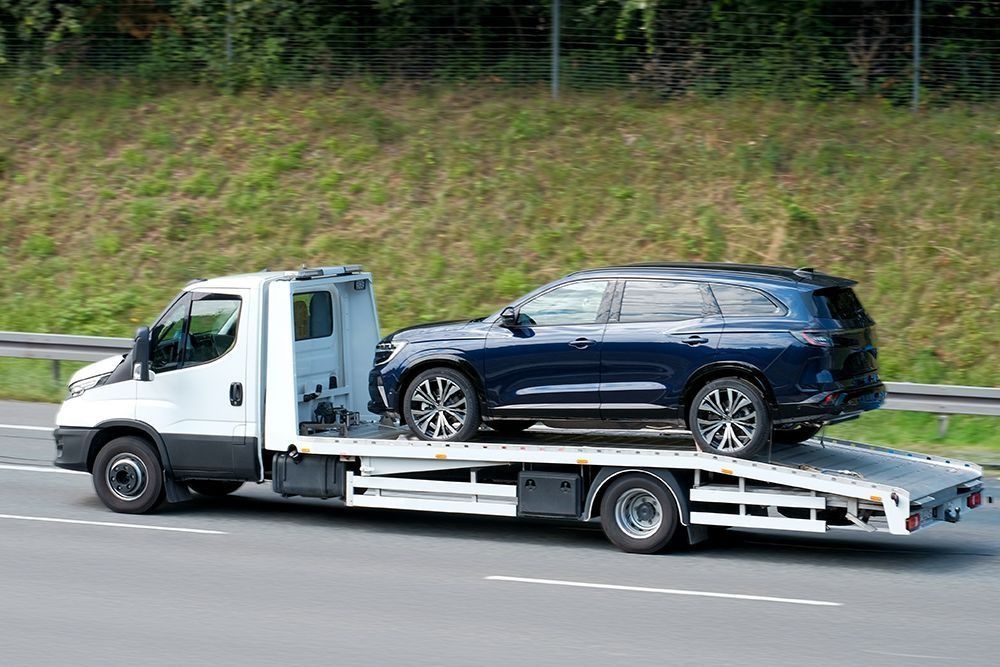 A tow truck is carrying a blue suv on a highway.