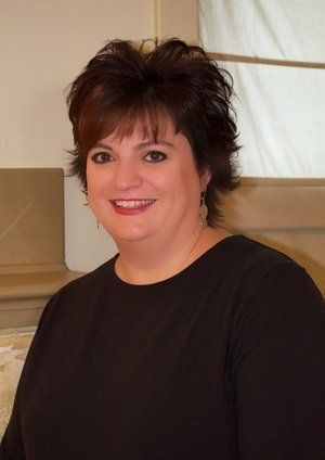 Woman with short, dark hair smiles. Wearing a black top in a neutral-toned room.