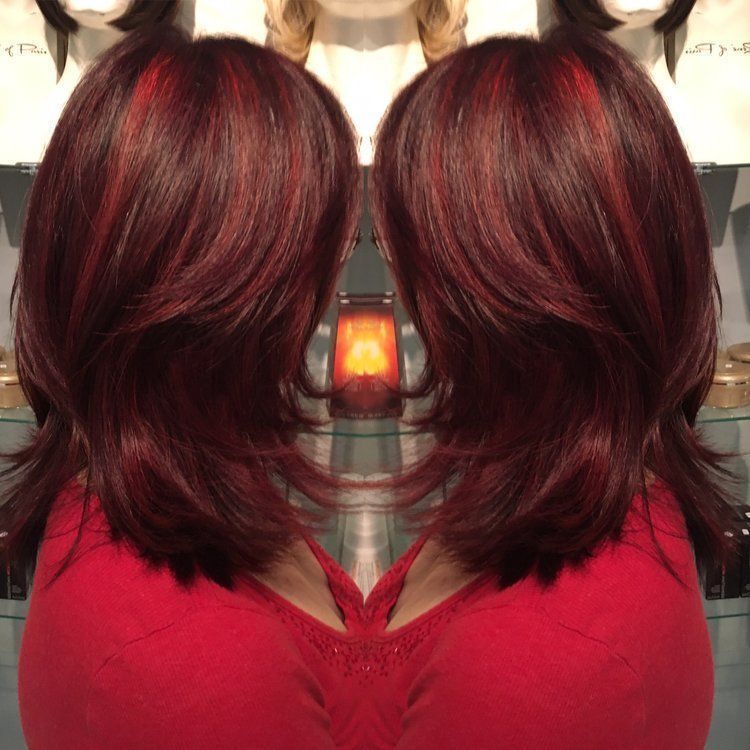 Woman with layered, reddish-brown hair with red highlights. Wearing a red top, indoors.