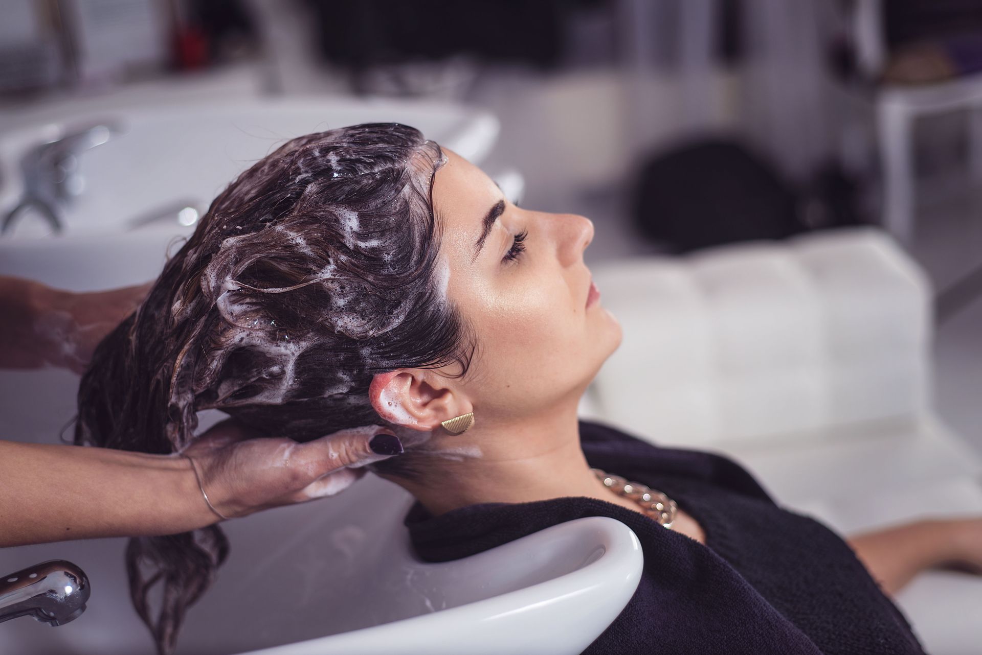 Woman having her hair washed at a salon, head tilted back, eyes closed.