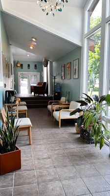 A bright waiting room with chairs, plants, and large windows. Soft blue walls, tile floor, and a water cooler.