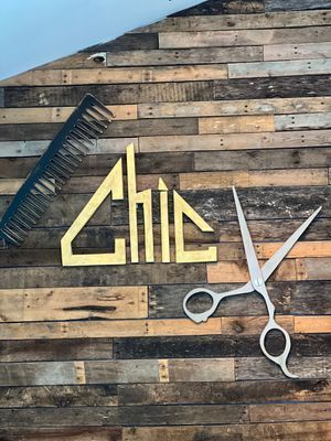 Gold "CHIC" sign with comb and scissors on a wood-paneled wall.