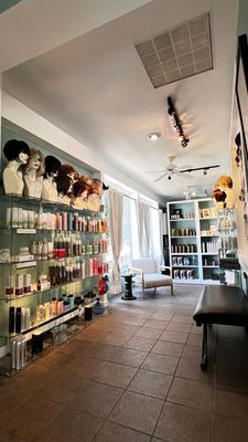 Hair salon interior with shelves of products, mannequins with wigs, and a waiting area.