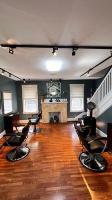 Hair salon interior with styling chairs, fireplace, wooden floors, and track lighting.