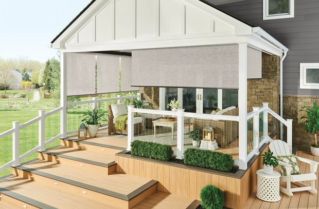 Covered backyard deck with outdoor seating, wood steps, white railing, and potted plants beside a house