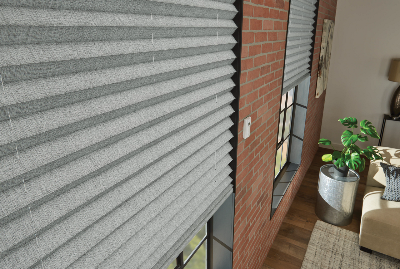 Close-up of gray window blinds beside a brick wall and a potted plant in a sunlit room.