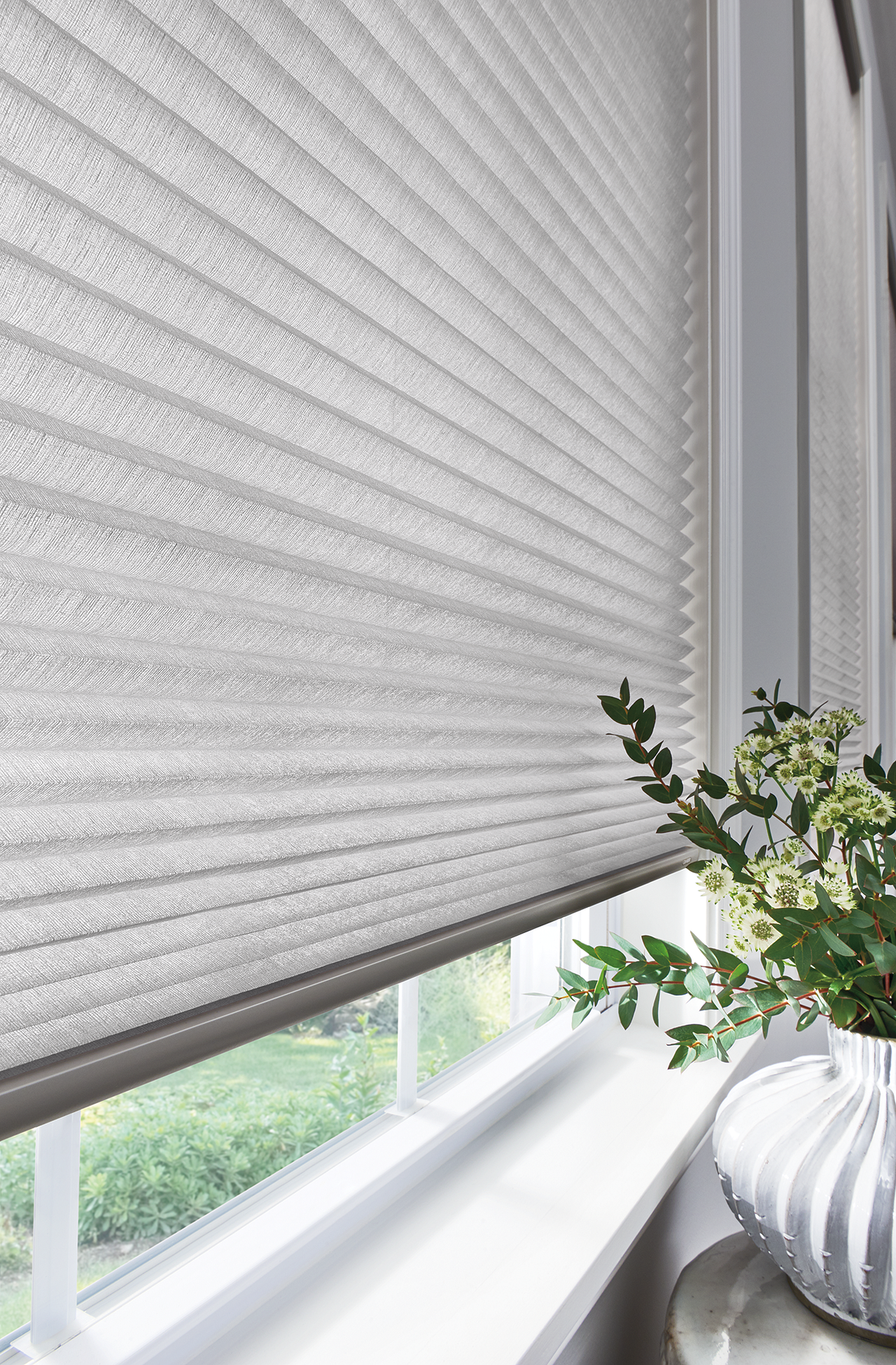 White window blind beside a windowsill with a potted green plant and soft daylight