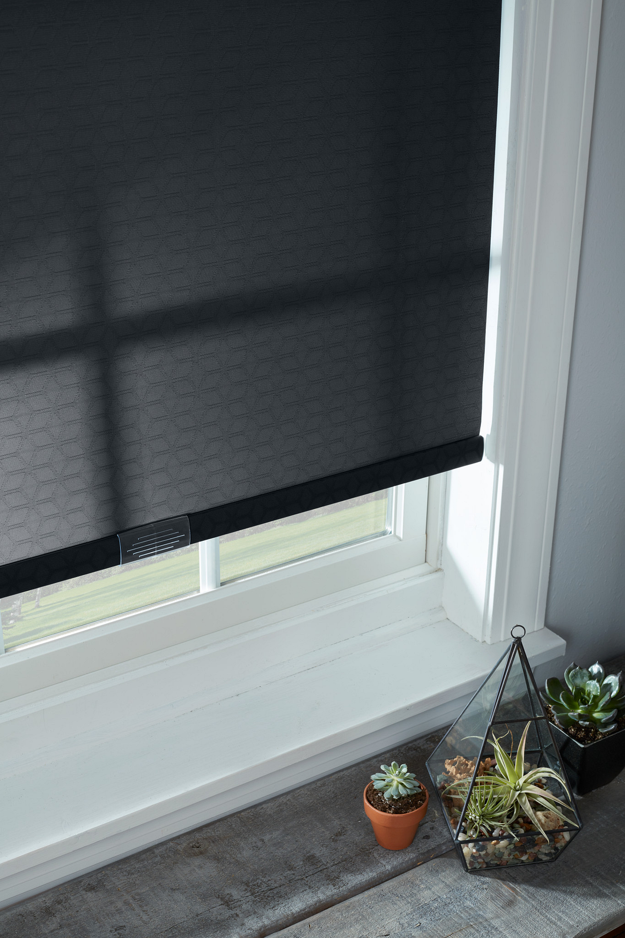 Black roller shade over a white windowsill with small potted succulents in the corner